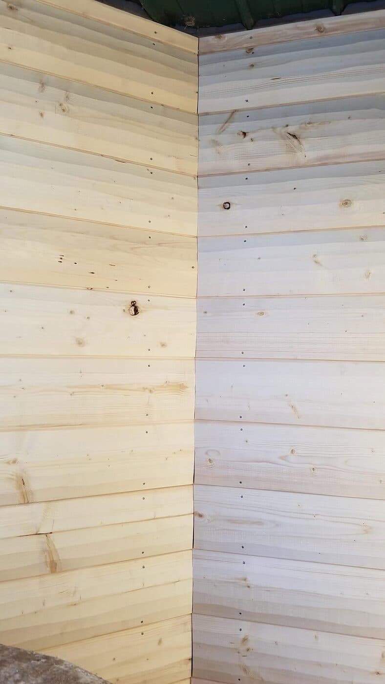 A tight outside corner of new natural-wood lap siding, two walls meeting in a clean mitered corner under a green metal soffit.