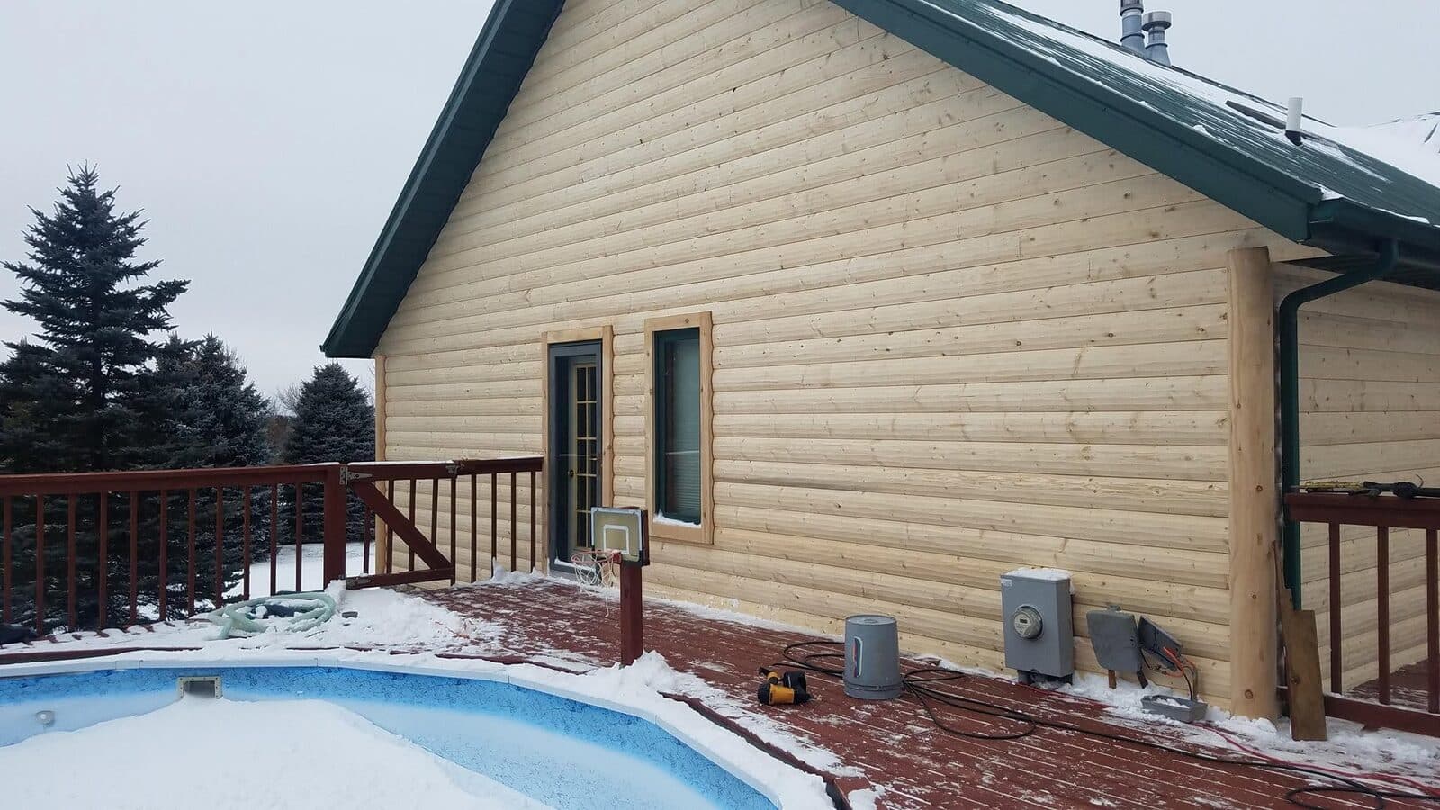 A gable end re-sided in fresh natural-wood lap under a green metal roof, above a stamped-concrete pool deck in winter.