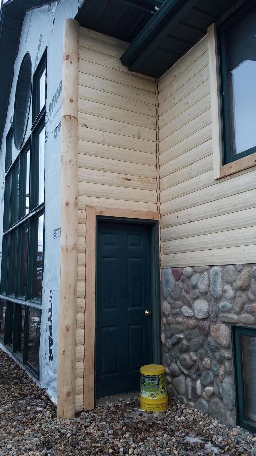A log-post corner with half-log siding above a river-rock stone wainscot.