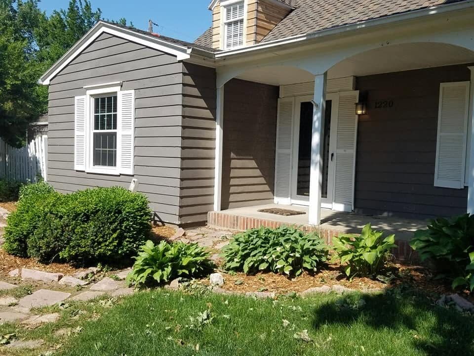 A finished home in greige lap siding with white-trimmed windows, a covered front porch, and tidy landscaping.