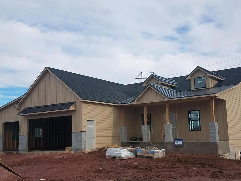 A finished home with charcoal architectural shingles and a black standing-seam metal accent roof over board-and-batten siding and a stone base.