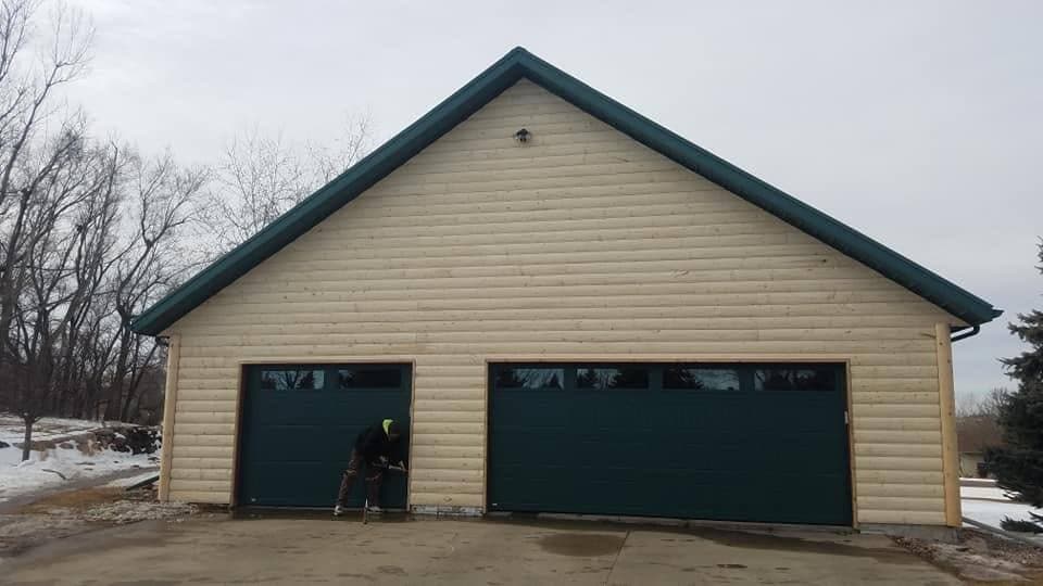 A green standing-seam metal roof and matching fascia over a log-sided garage with green overhead doors.