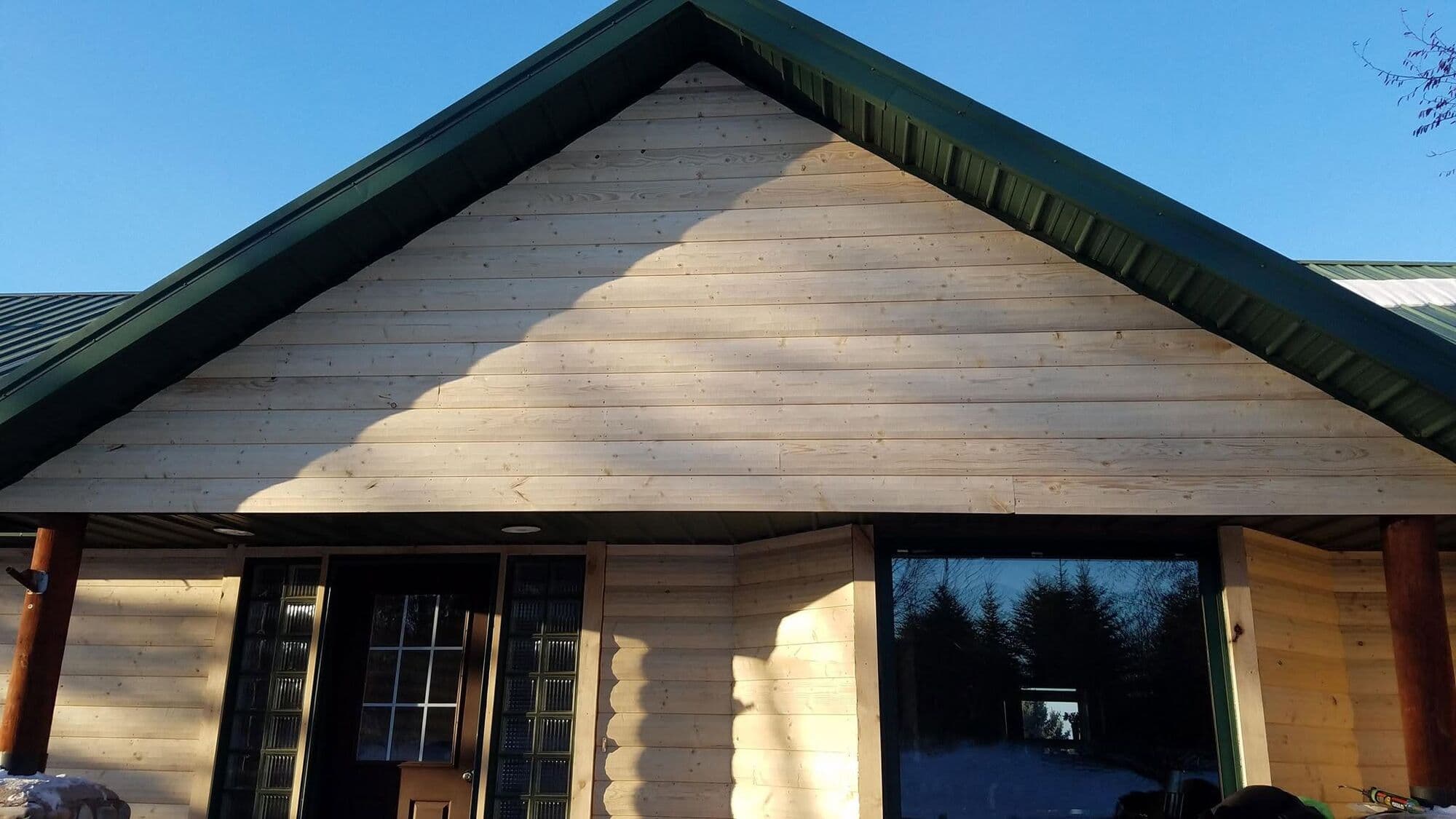 A finished home with fresh natural-wood lap siding and a dark green metal roof, gable end over log porch posts.
