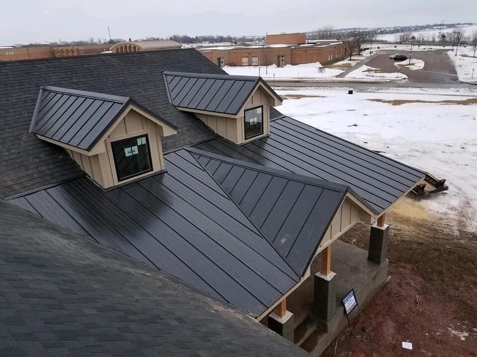 A dark standing-seam metal roof with matching gable dormers on a finished home.