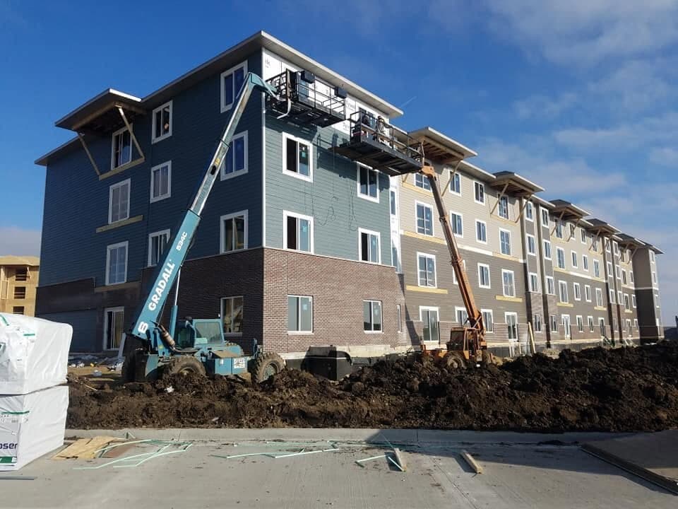 A four-story apartment complex being re-sided, two telehandlers reaching the upper floors.